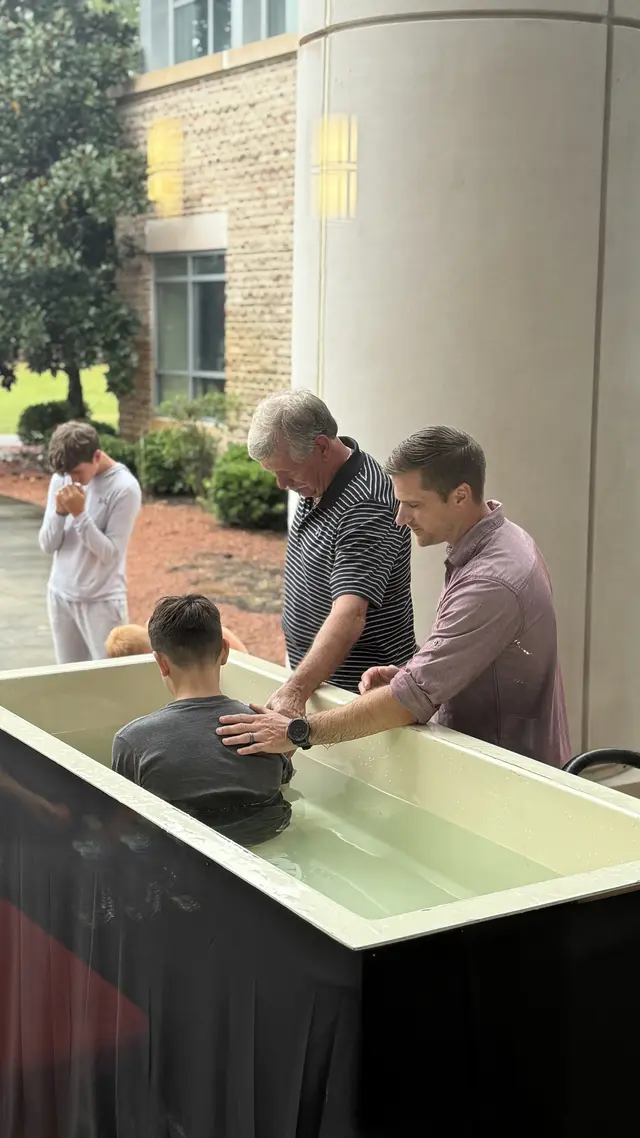 A child being baptized with family gathered around the baptistry